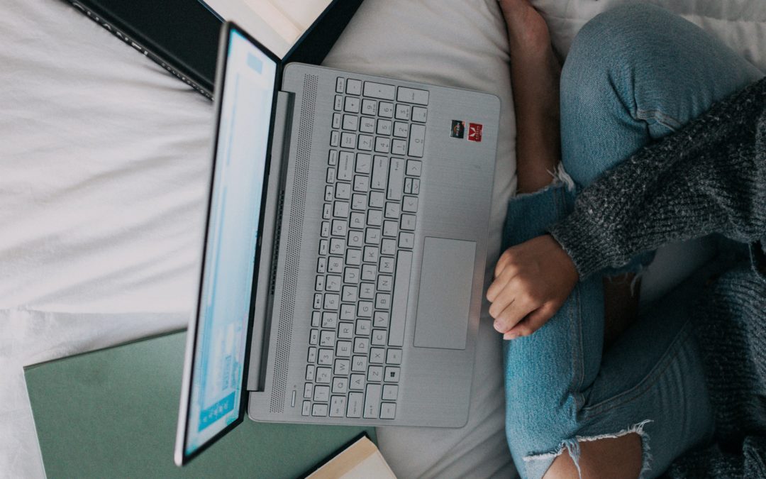Person sitting in front of books, papers, and computer sprawled on bed