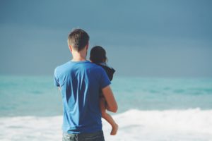 Father holding child, both are looking out to sea