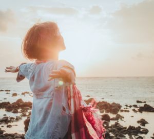 Woman with arms spread facing a sunrise over the ocean