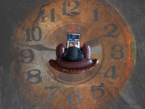 Someone sitting in a chair working on their laptop. The chair is on top of a clock.