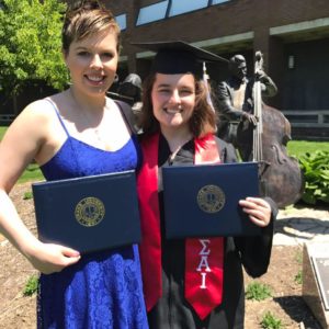 Caitlin and Jessica, in cap in gown,holding their college diplomas on the day Jessica graduates from Drake University