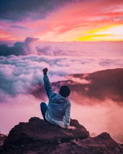 Man on a mountaintop looking at the sunrise with his fist in the air