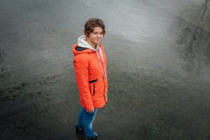 Woman in rain gear standing on a grey shore in the fog