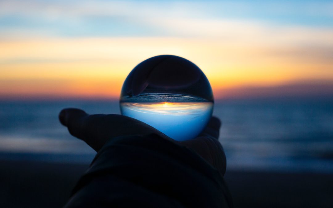 Hand holding a crystal ball which inverts the sunset