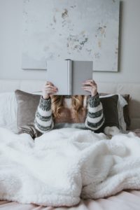 A woman in bed holding a book up while she reads.