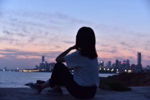 Woman sitting on shore looking across a body of water to a city