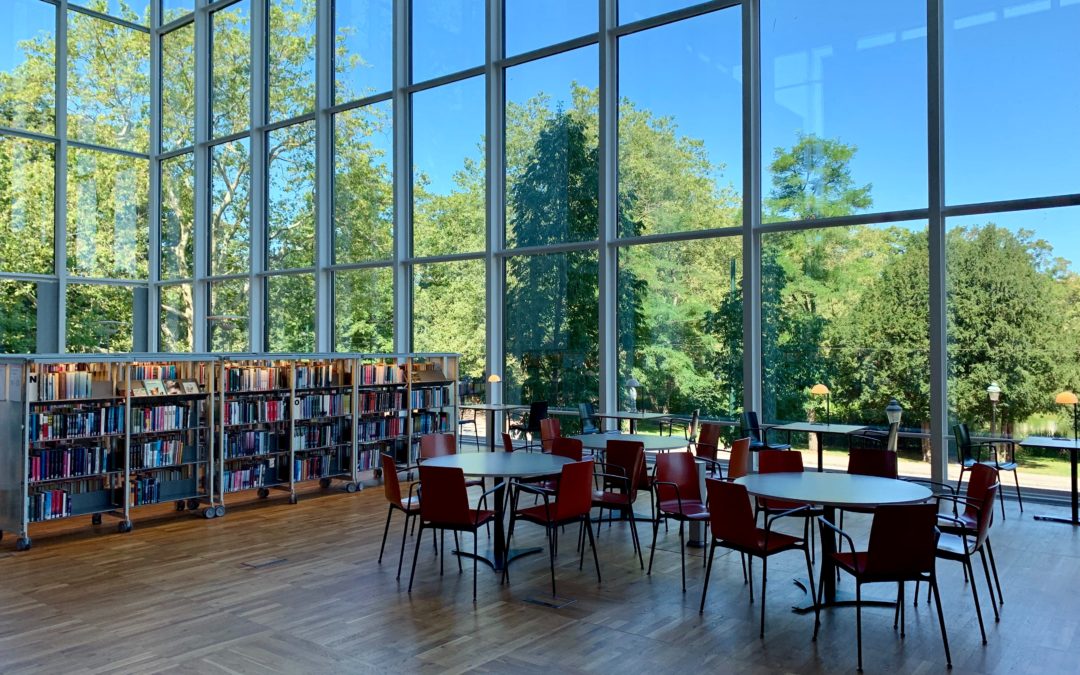 Tables and book cases in a large glass-enclosed room with a beautiful view