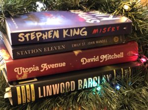 Stack of books surrounded by greenery and Christmas lights