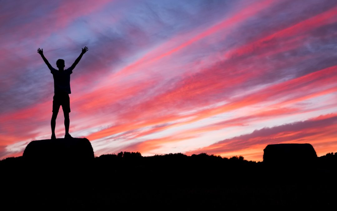Person with raised arms on mountain top against a setting sun