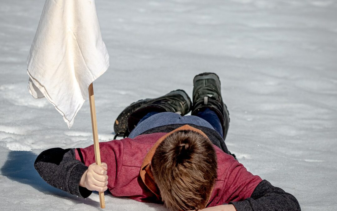 Person lying facedown in the snow holding a white flag