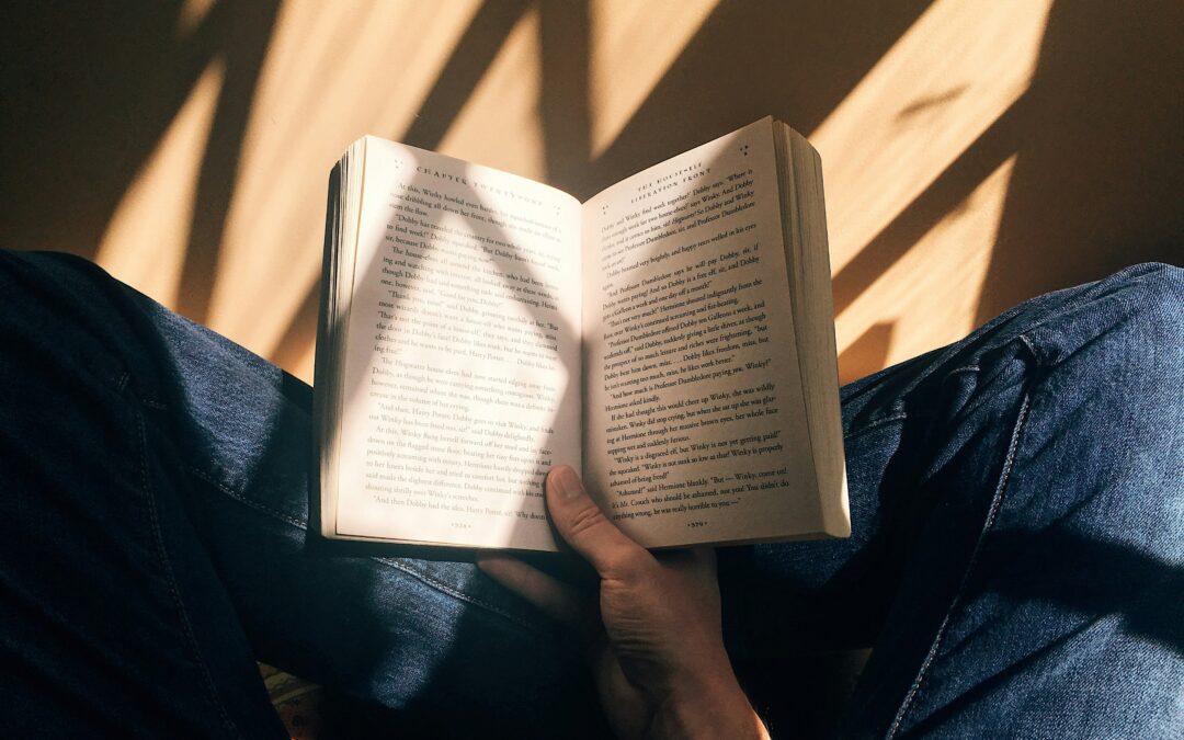 Hand holding open book over crossed legs